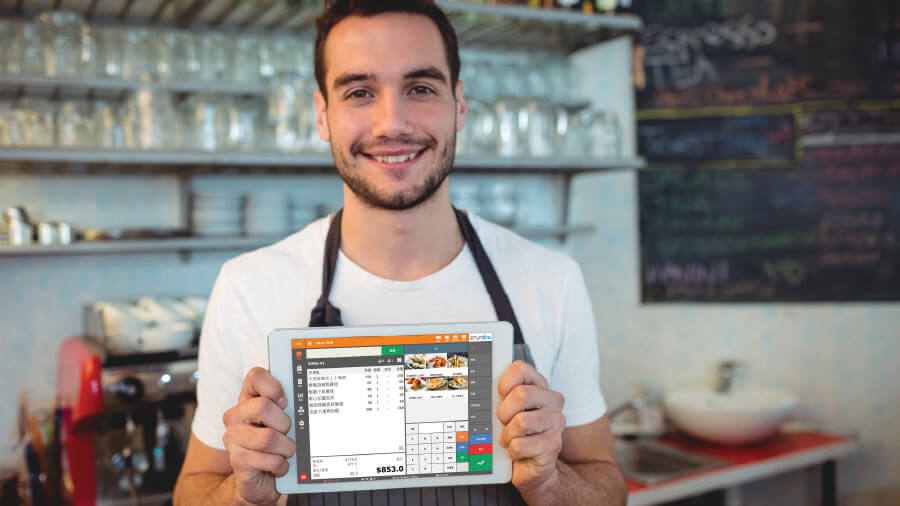 A confident male shop owner smiling while holding a tablet computer, representing a reliable store management solution with eRunlite POS system and 24/7 customer support.