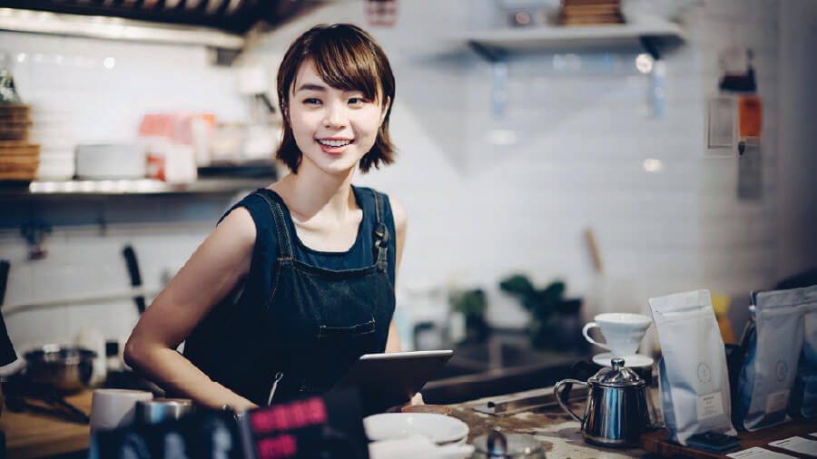 A smiling female shop owner holding a tablet, managing her small cafe using eRunlite POS system on the service counter.